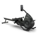 A sleek, black rowing machine with a padded seat, footrests, handlebars, and a digital display screen, set against a plain white background. The brand TRUE is visible on the side.