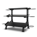 Black, two-tiered gym equipment rack with sturdy legs, raised top shelf, and side hooks for accessories, designed for organizing weights or fitness gear against a plain white background.